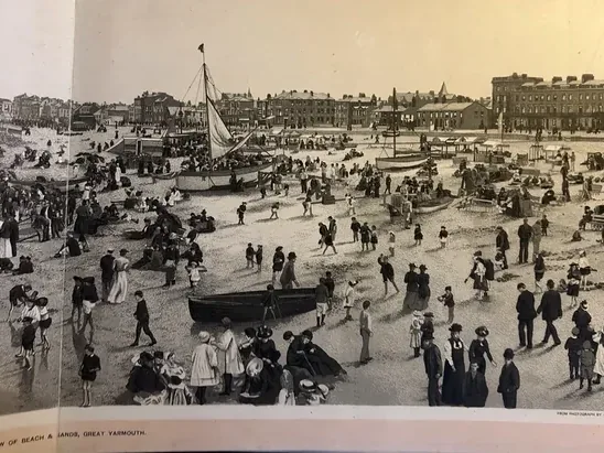 Open photographic album spread showing a crowded Edwardian beach and sands at Great Yarmouth, with boats, children and promenaders along the shore