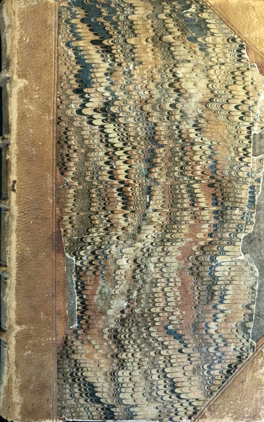 A worn nineteenth-century half-leather book with marbled-paper boards, a rubbed spine and damaged leather corners.