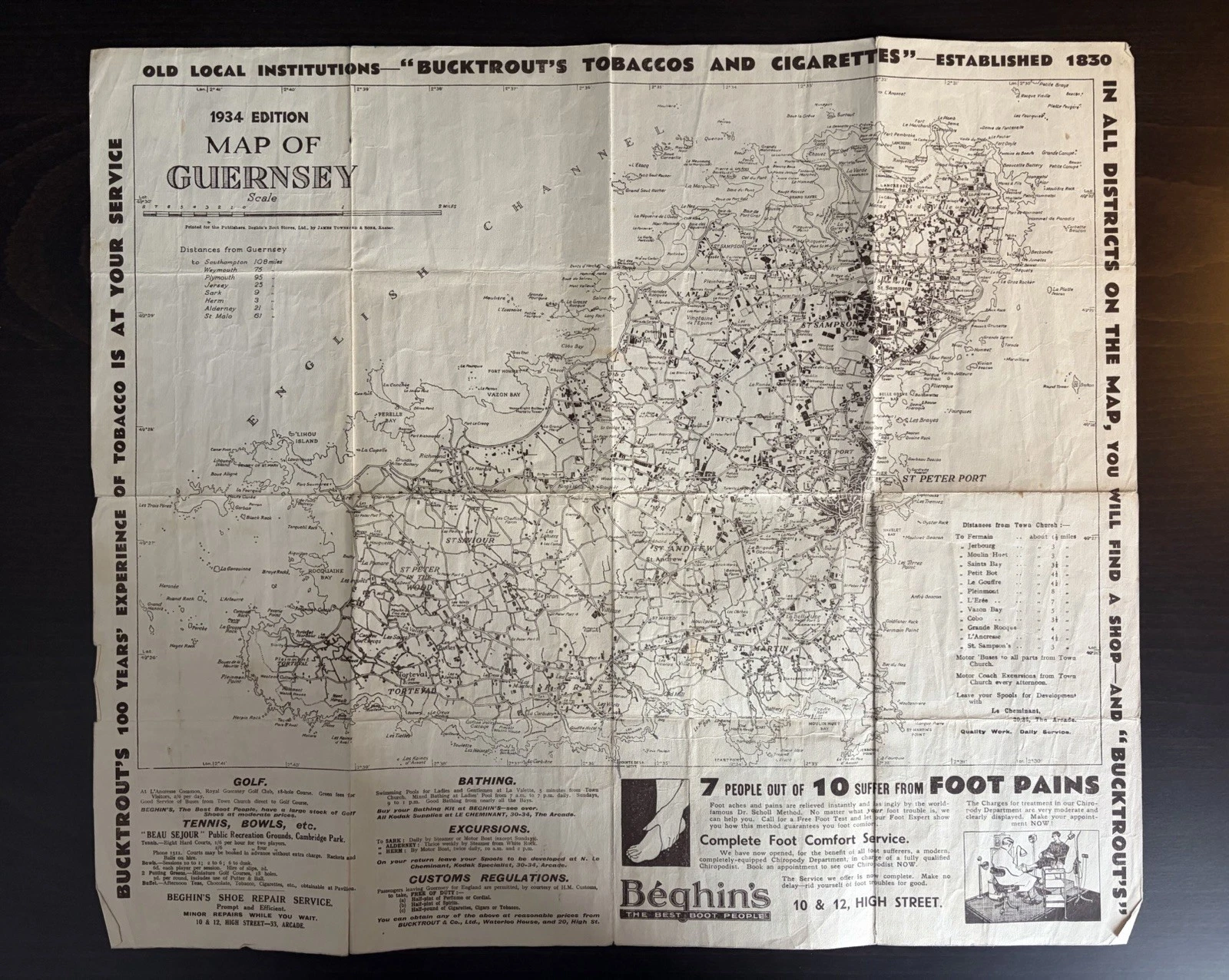Complete black-and-white 1934 map of Guernsey surrounded by visitor information and advertisements for Bucktrout tobacco and Beghin's footwear.