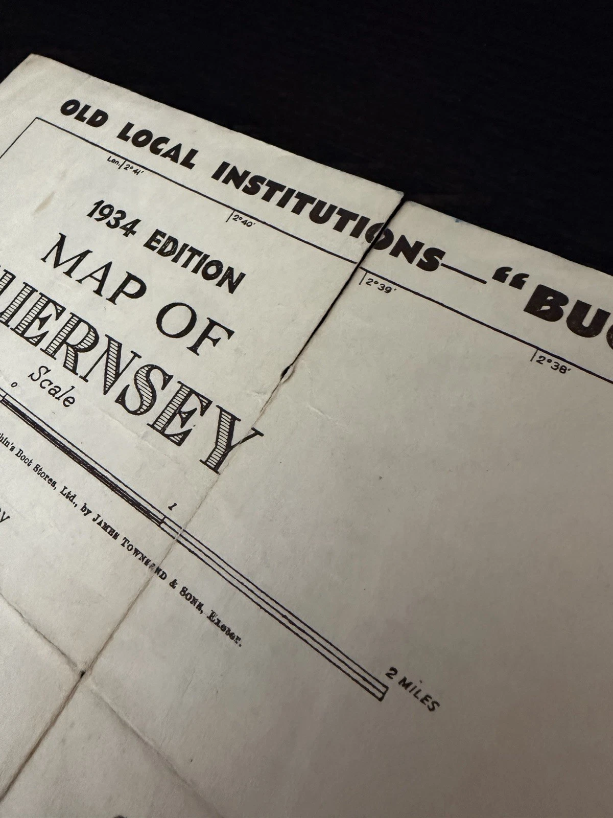 Angled close view of the 1934 Guernsey map title showing intersecting folds, toning, handling and a small hole at the fold intersection.