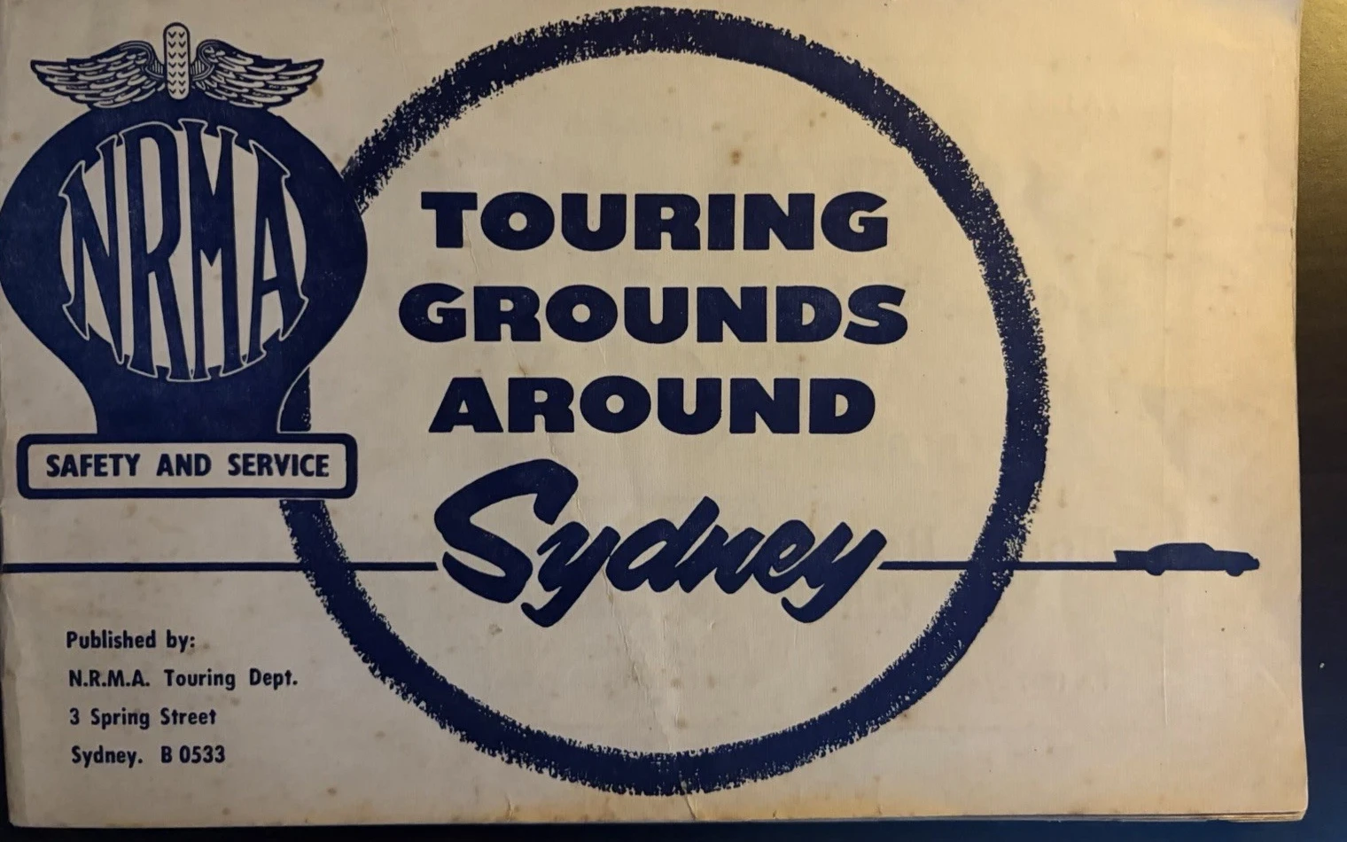 Cream and dark-blue NRMA Touring Grounds Around Sydney cover with a winged badge, circular brushstroke and small car silhouette.